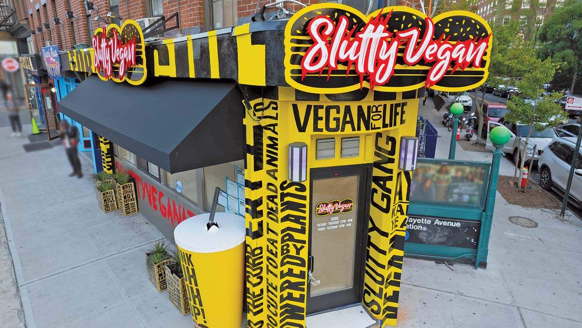 The Slutty Vegan storefront in yellow and black with its neon sign, on a city street.